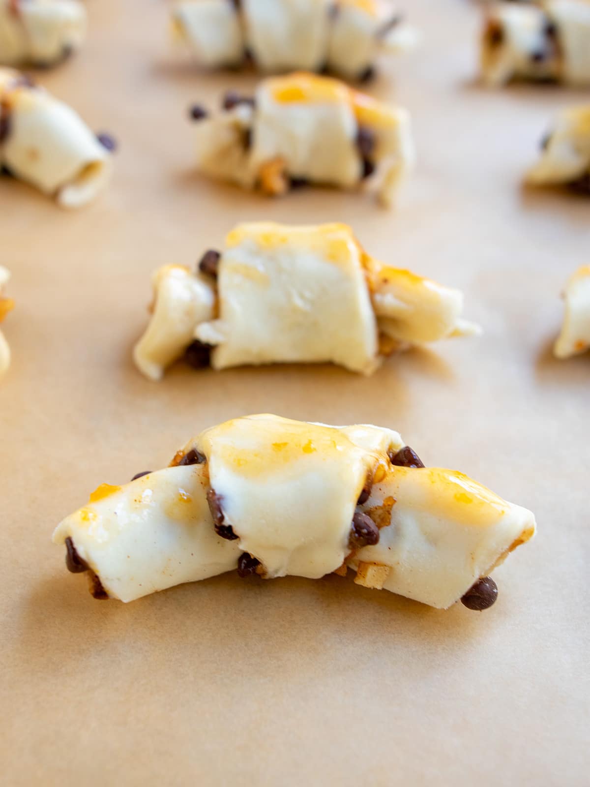 Close up of unbaked rugelach with apricot jam brushed on top resting on parchment paper.