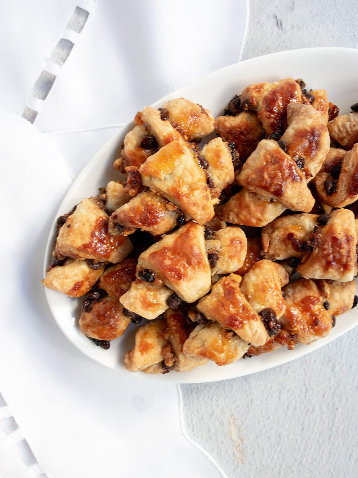 A white plate of rugelach on a white shiny table runner.