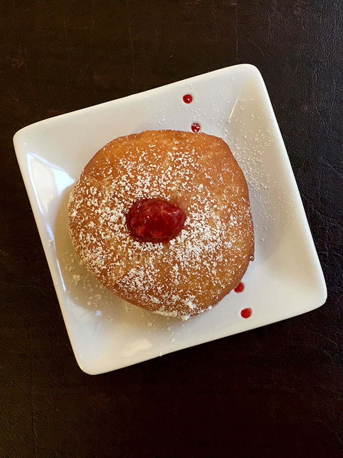 A soufganiyot (round jelly doughnut) on a white plate with powdered sugar.