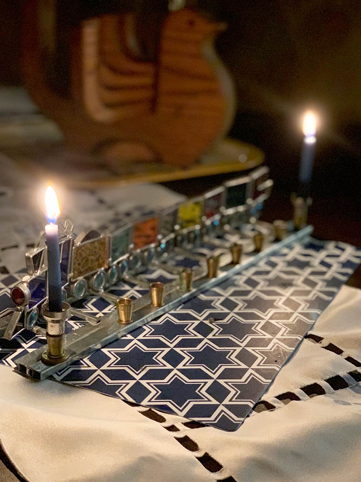 2 hanukkiah with one lit in the foreground.