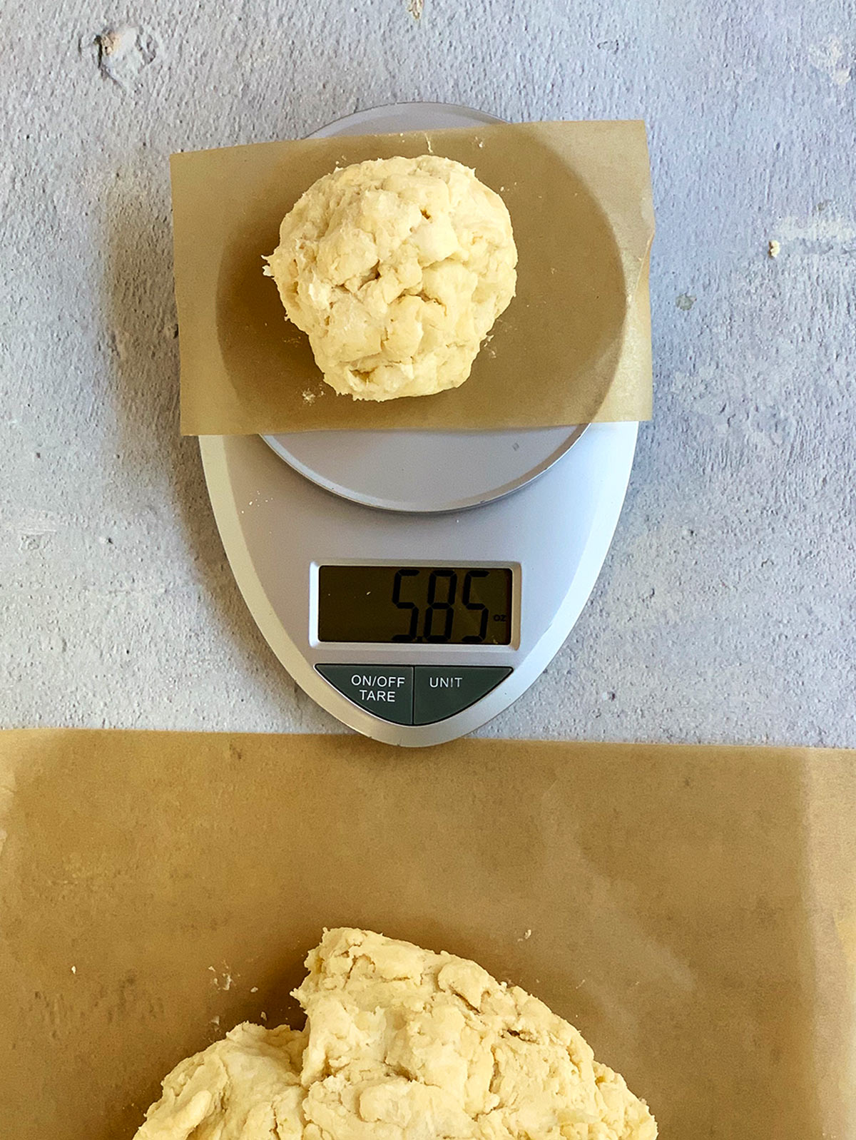 One dough ball measured on a scale to 5.85 ounces. More dough to the side, waiting to be weighed.