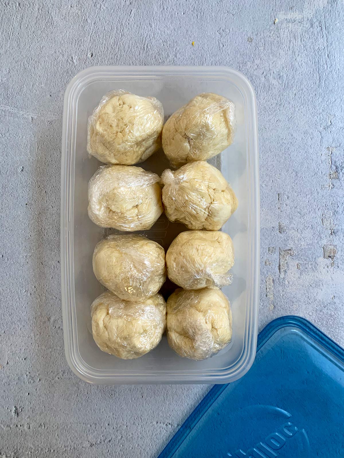 8 dough balls wrapped in plastic and placed in a container ready to refrigerate.