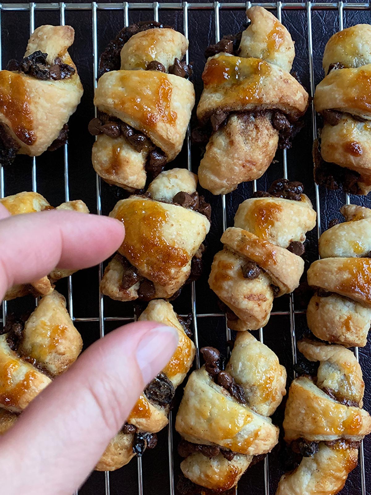 Baked rugelach on cooling rack with a hand reaching for one.