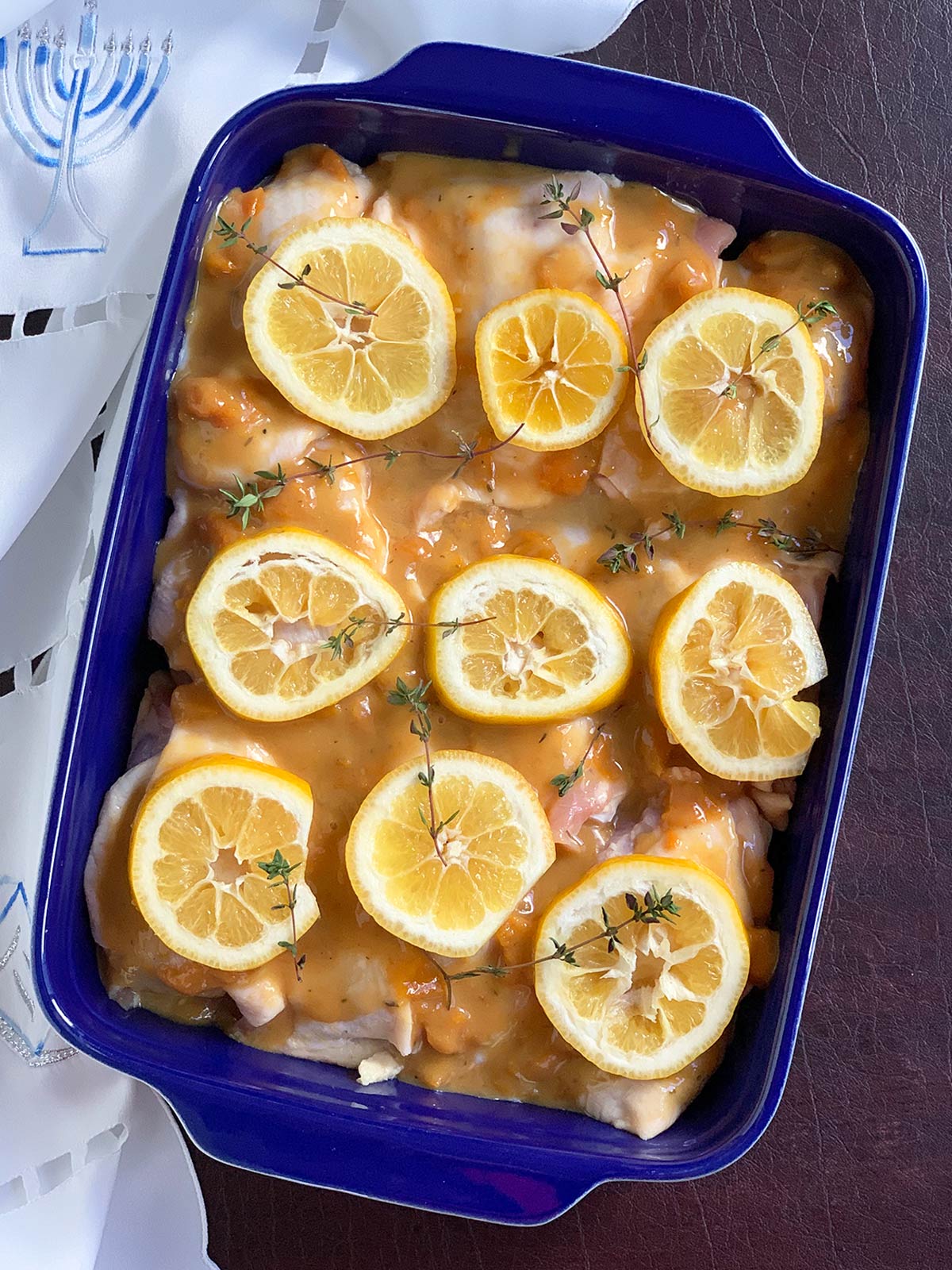 Prepped chicken in blue pan with sauce and lemons on top, ready to bake.