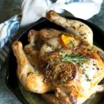 Whole roasted chicken in a cast iron pan on a kitchen towel.