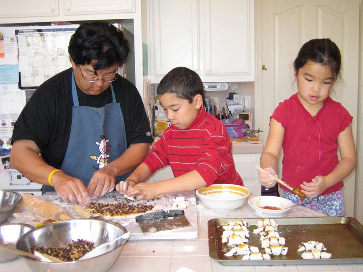 Dad and two kids making rugelach on a kitchen counter.