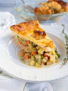 Slice of turkey pot pie in a white plate with the whole pot pie in the background.