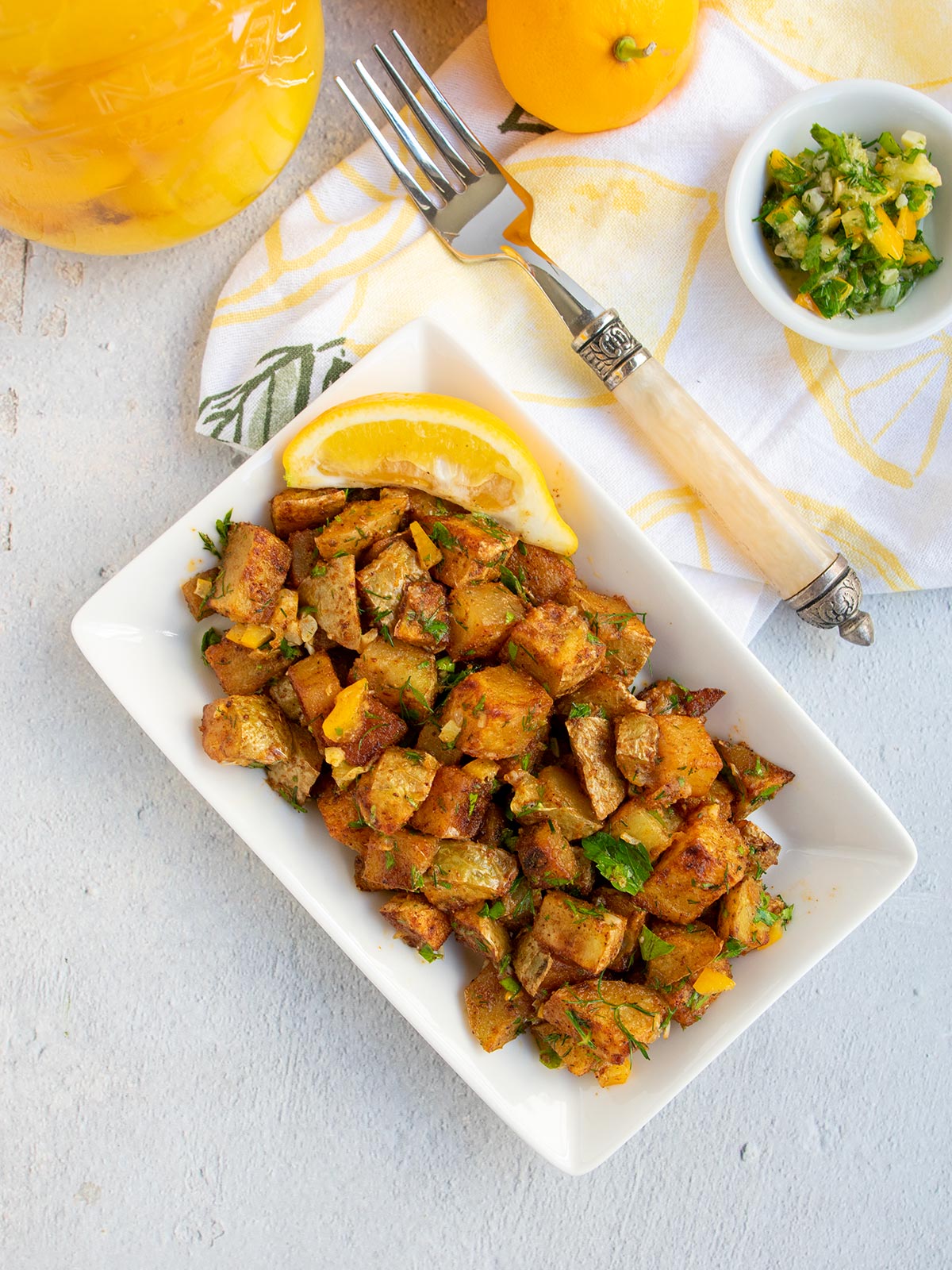 Roasted Harissa Potatoes with Preserved Lemon Herb topping on a white plate with sliced fresh lemon.