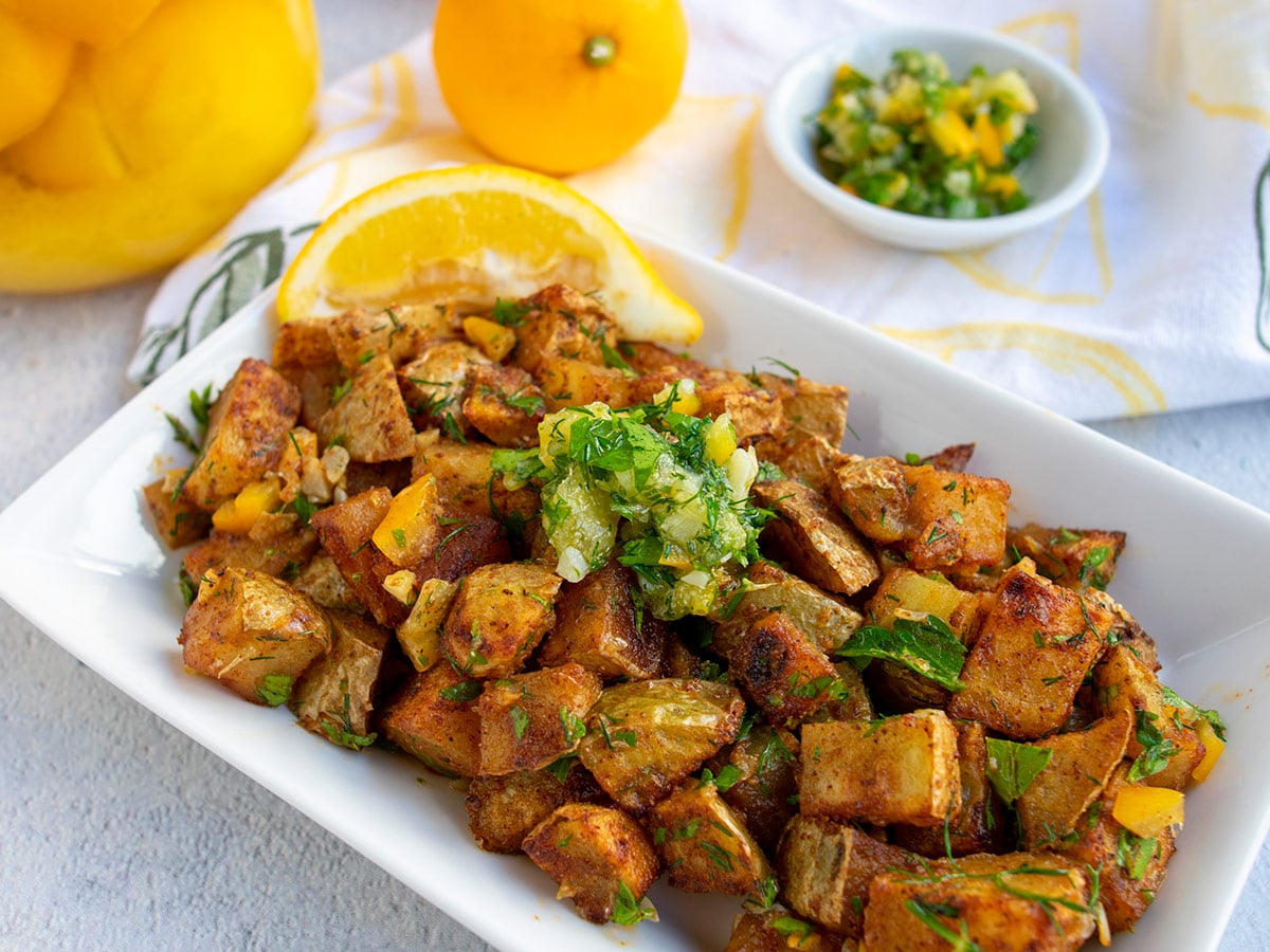 harissa potatoes on white plate at an angle with a slice of fresh lemon and gremolata on top