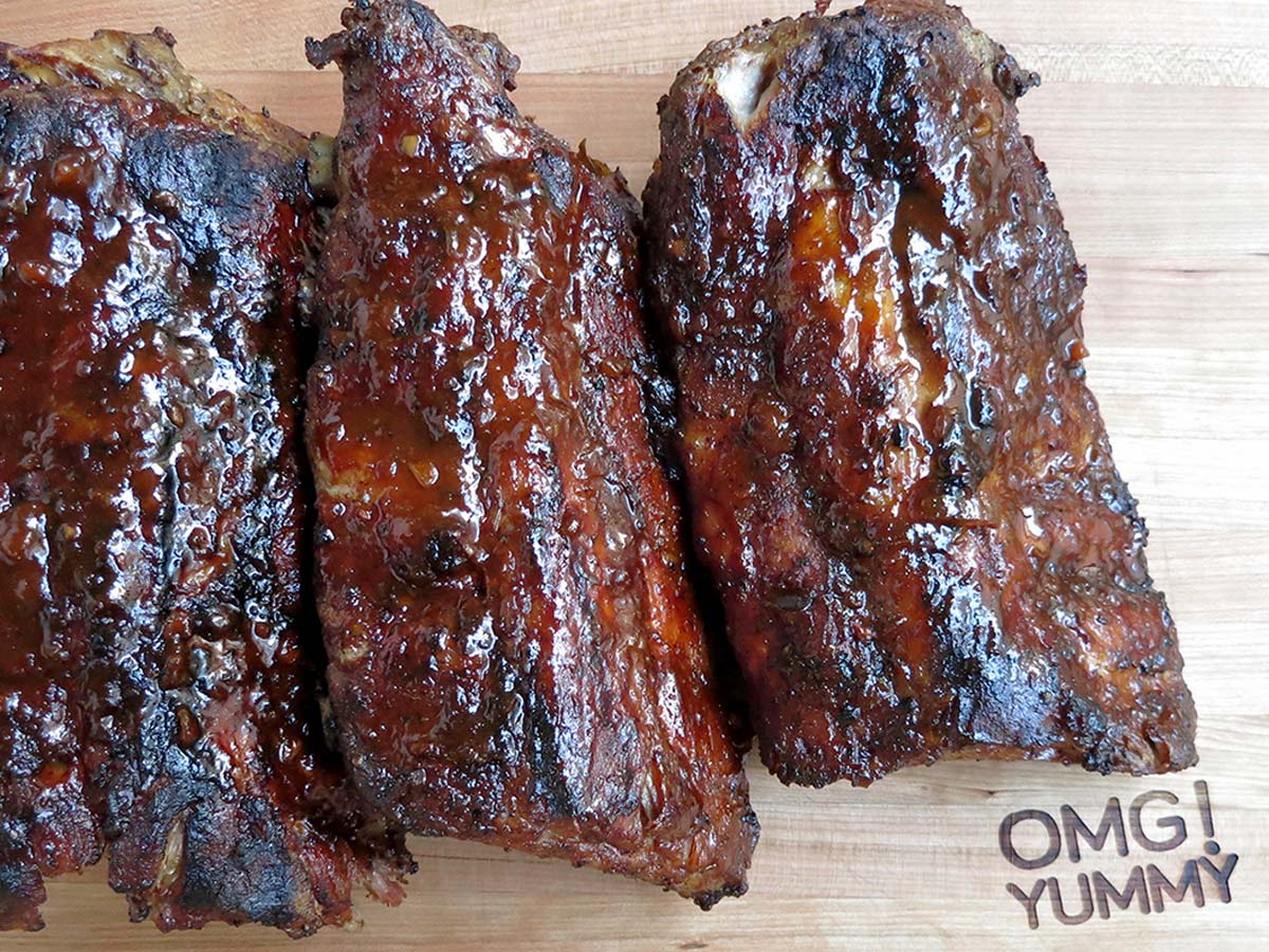 Finished rib racks with barbecue sauce on a cutting board engraved with OMG! Yummy.