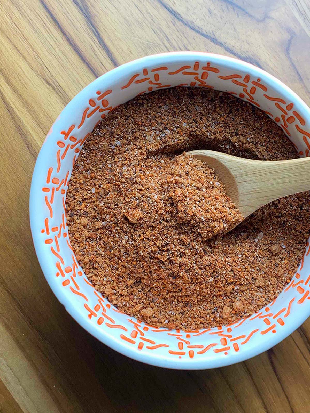 Dry spice rub in orange bowl with a wooden spoon.