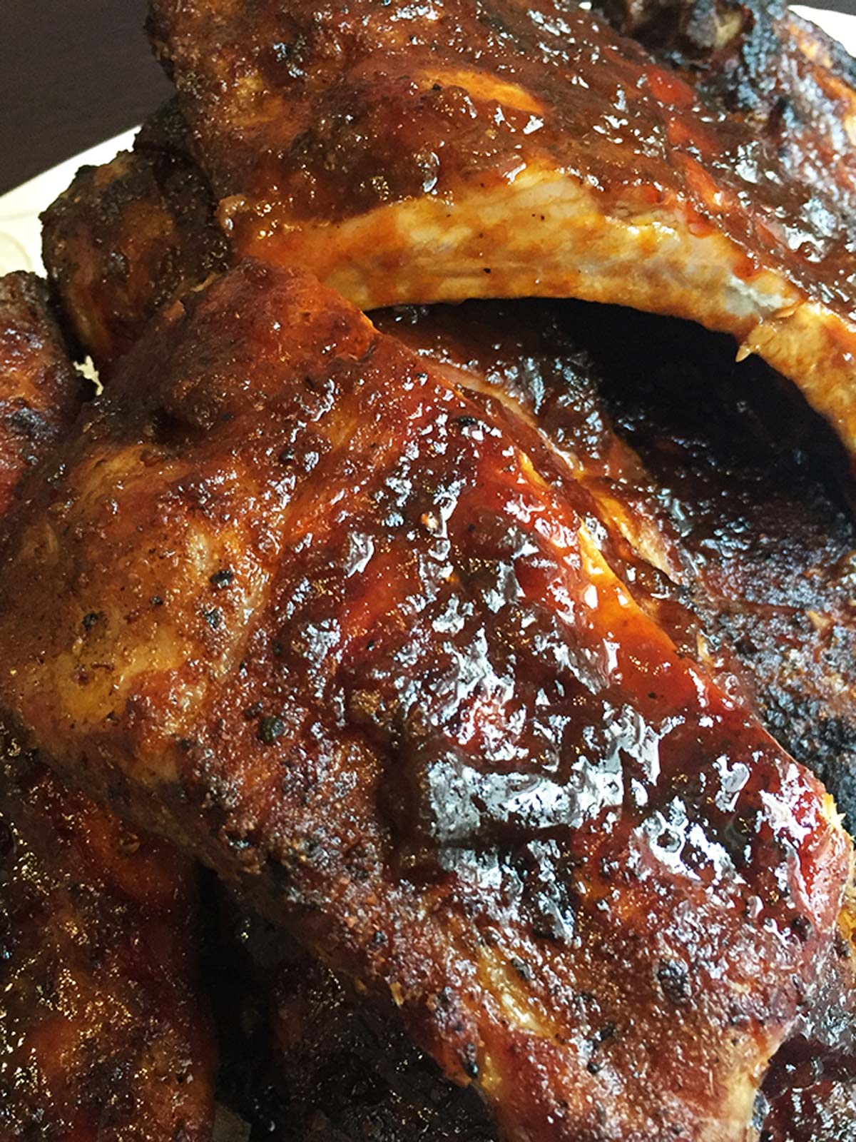 Finished ribs on white plate with barbecue sauce ready to be cut and serve.