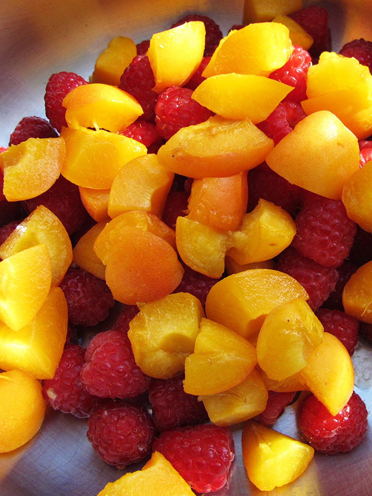 Chopped apricots and raspberries in pot with lemon juice ready to cook.