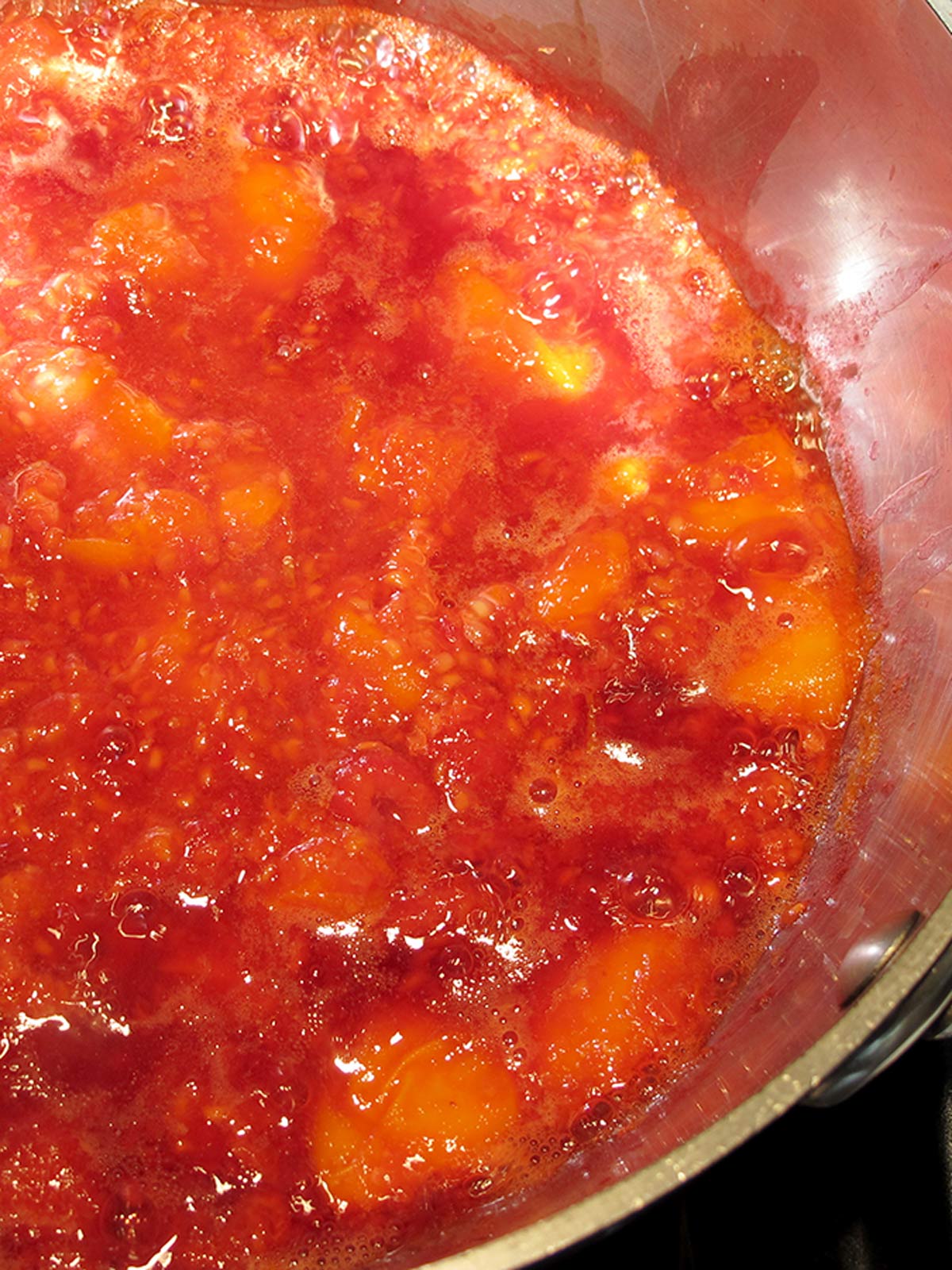 Apricots and raspberries bubbling in pot.