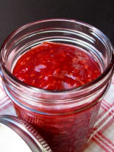 Apricot raspberry jam in a glass jar on a red checked napkin.