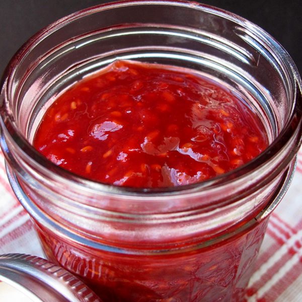 Apricot raspberry jam in a glass jar on a red checked napkin.