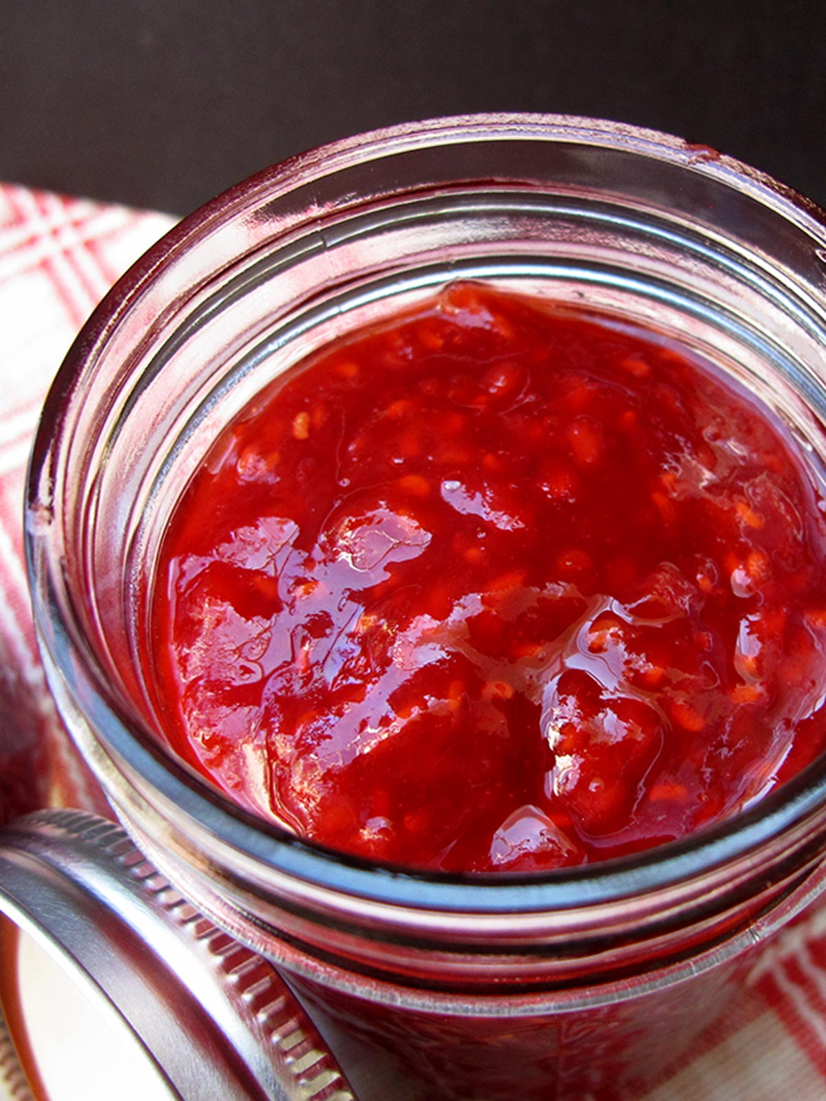 Close-up of apricot raspberry jam in jar with can lid leaning on jar.
