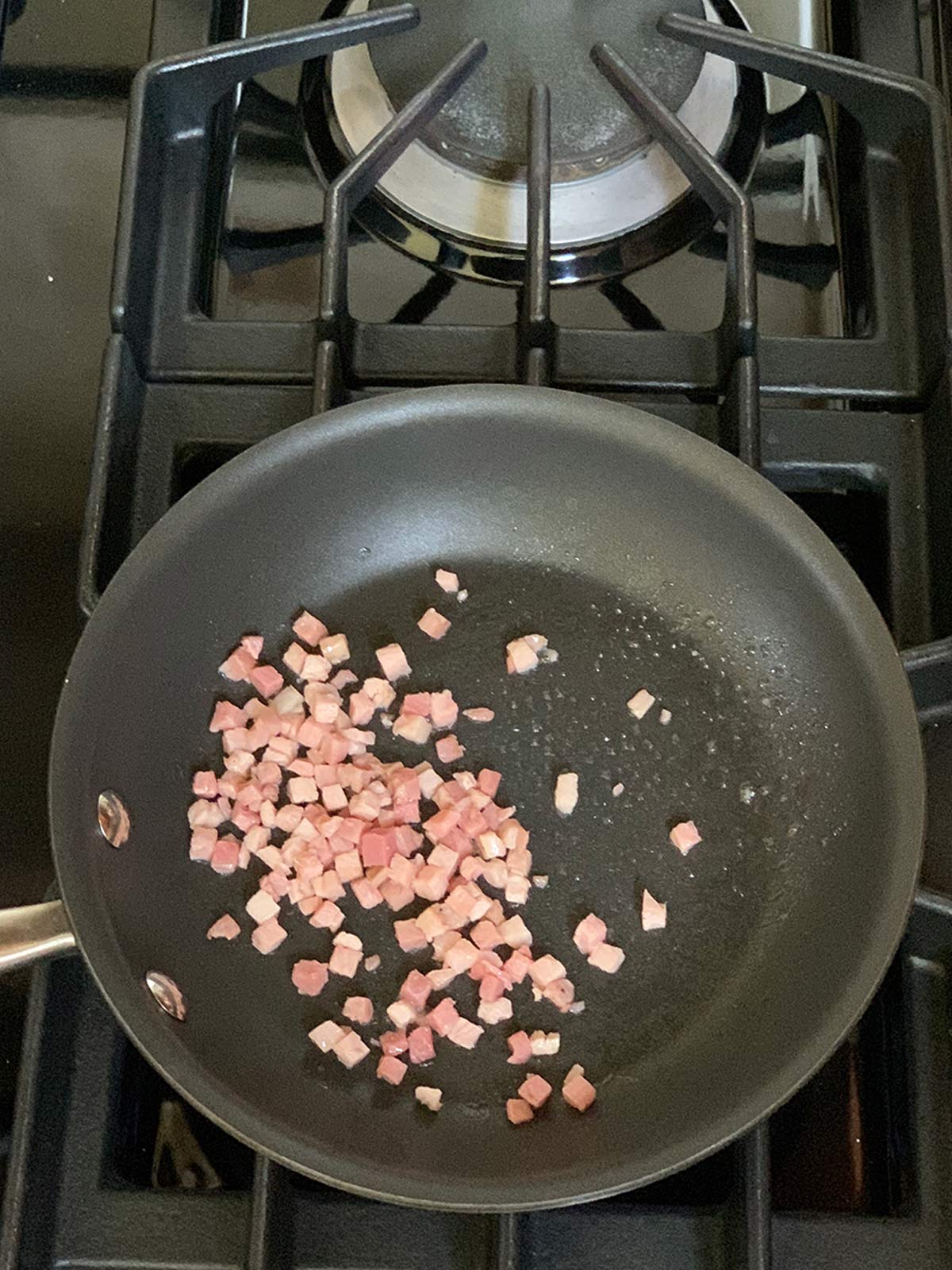 Pancetta cubes cooking in sauté pan on the stove.