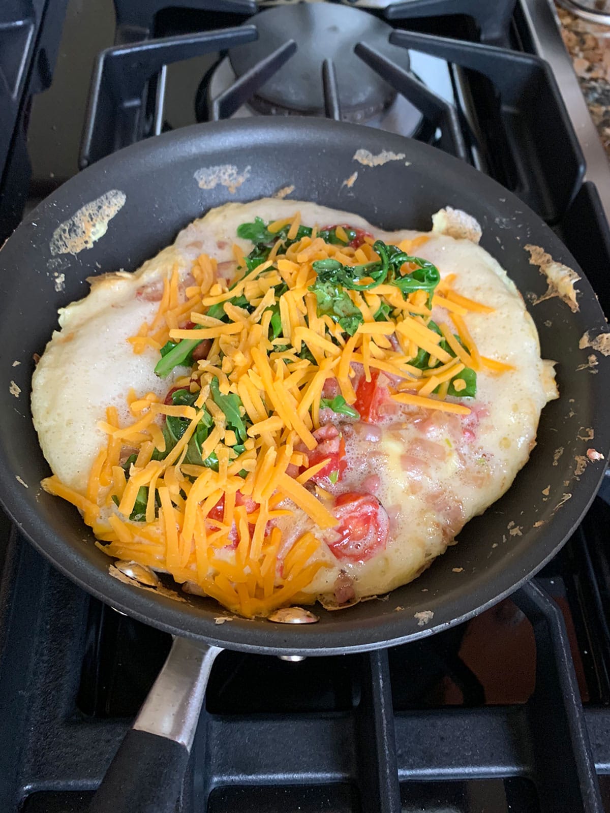 Omelette in pan with fillings layered on top in a sauté pan cooking on the stove.