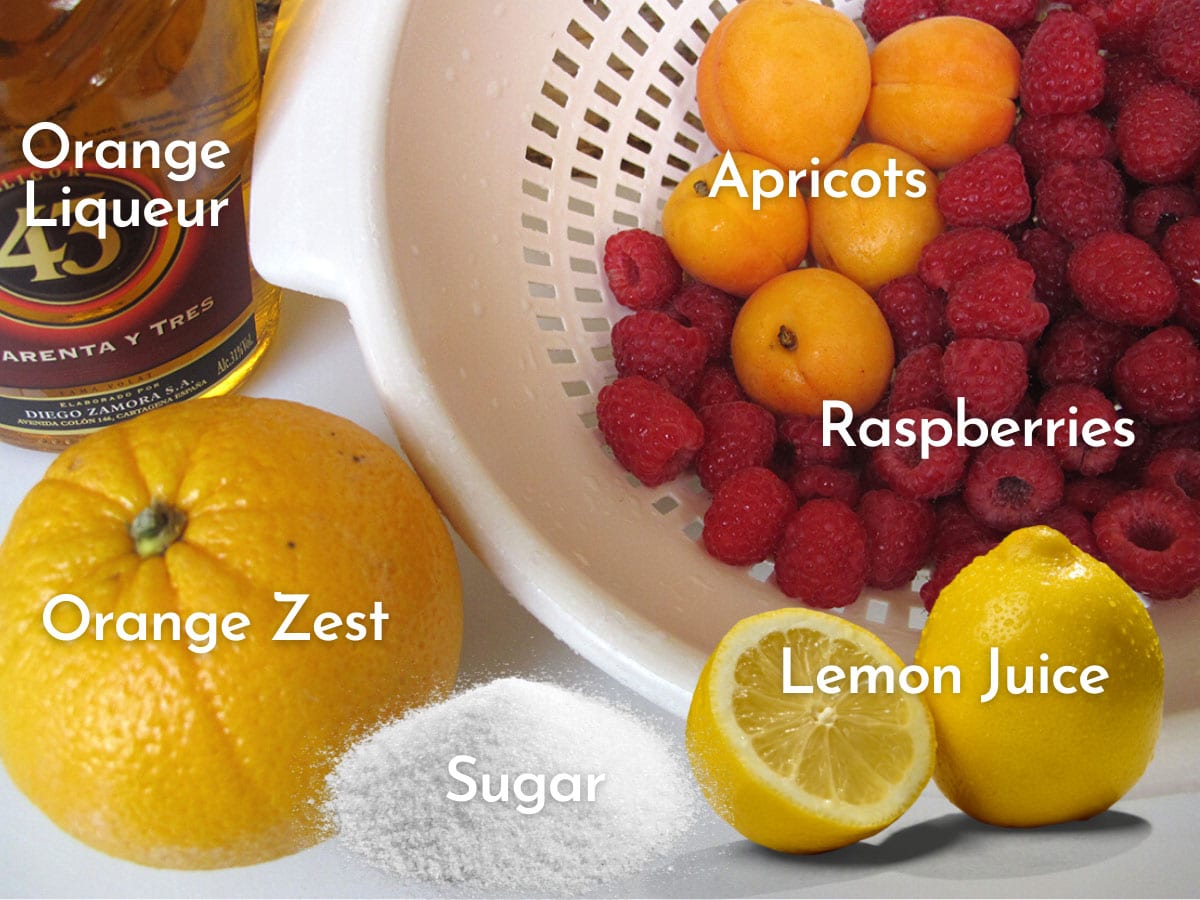 A colander filled with ripe apricot, fresh raspberries and to the side a fresh orange for zest and a bottle of  Mexican liqueur called 43 with labels to describe in white.