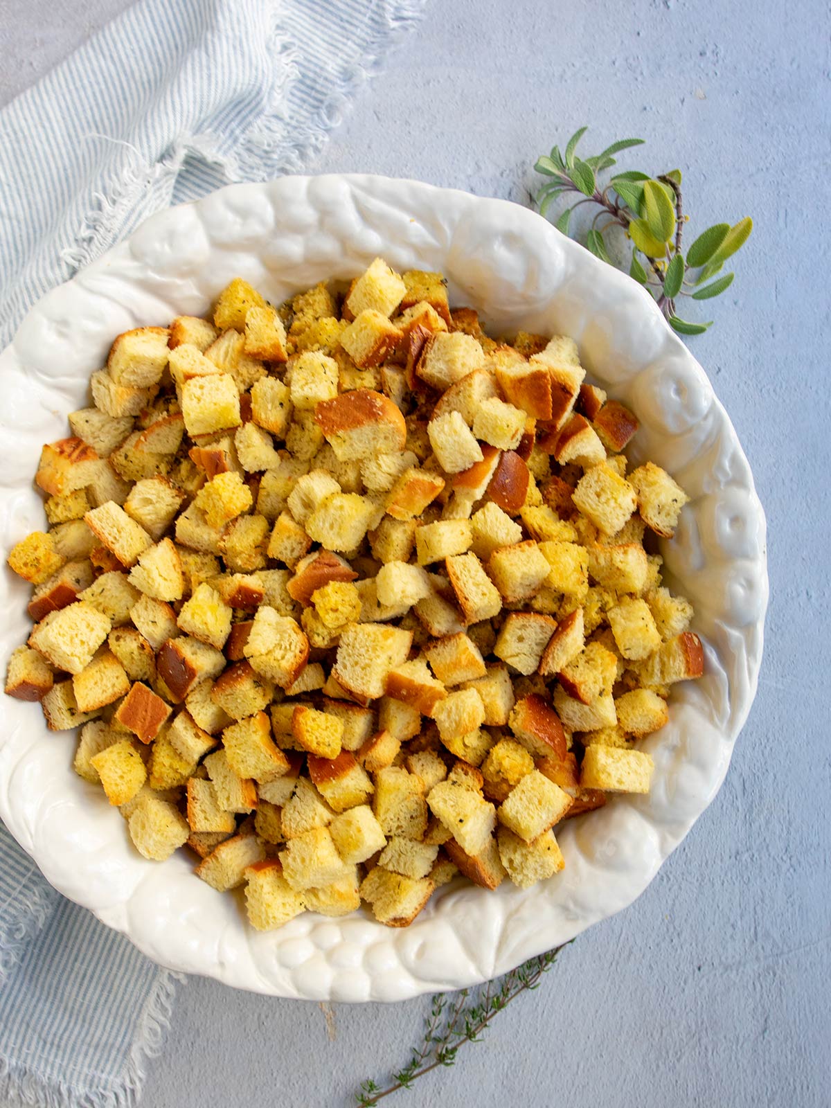 Large white bowl with baked stuffing cubes with fresh herbs and a striped napkin nearby.