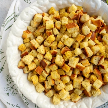 Large white bowl with cornbread and challah bread cubes for stuffing plus fresh herbs and an herb napkin on the side.