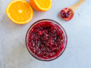 Jar of jam with sliced orange and spoon of jam in the background.