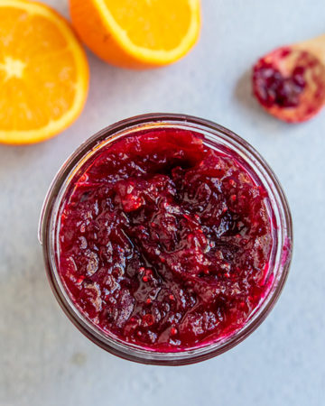 Jar of jam with sliced orange and spoon of jam in the background.
