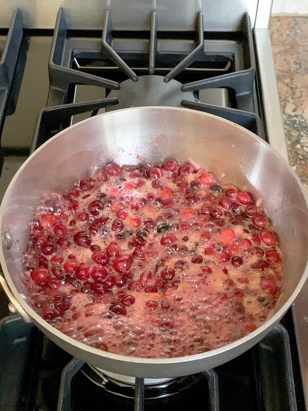 Cranberry jam boiling on stove top in a medium sized pot.