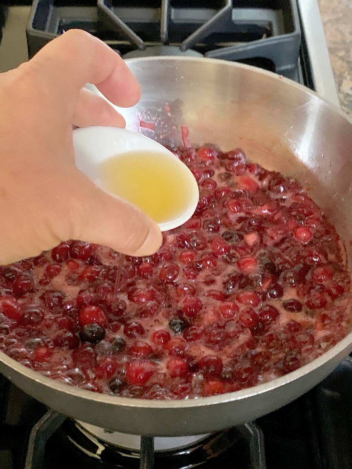 Hand showing pouring the liqueur into the orange cranberry jam in the pot.