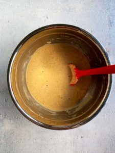 Pumpkin Spice pancake batter in stainless bowl with a red spoon.
