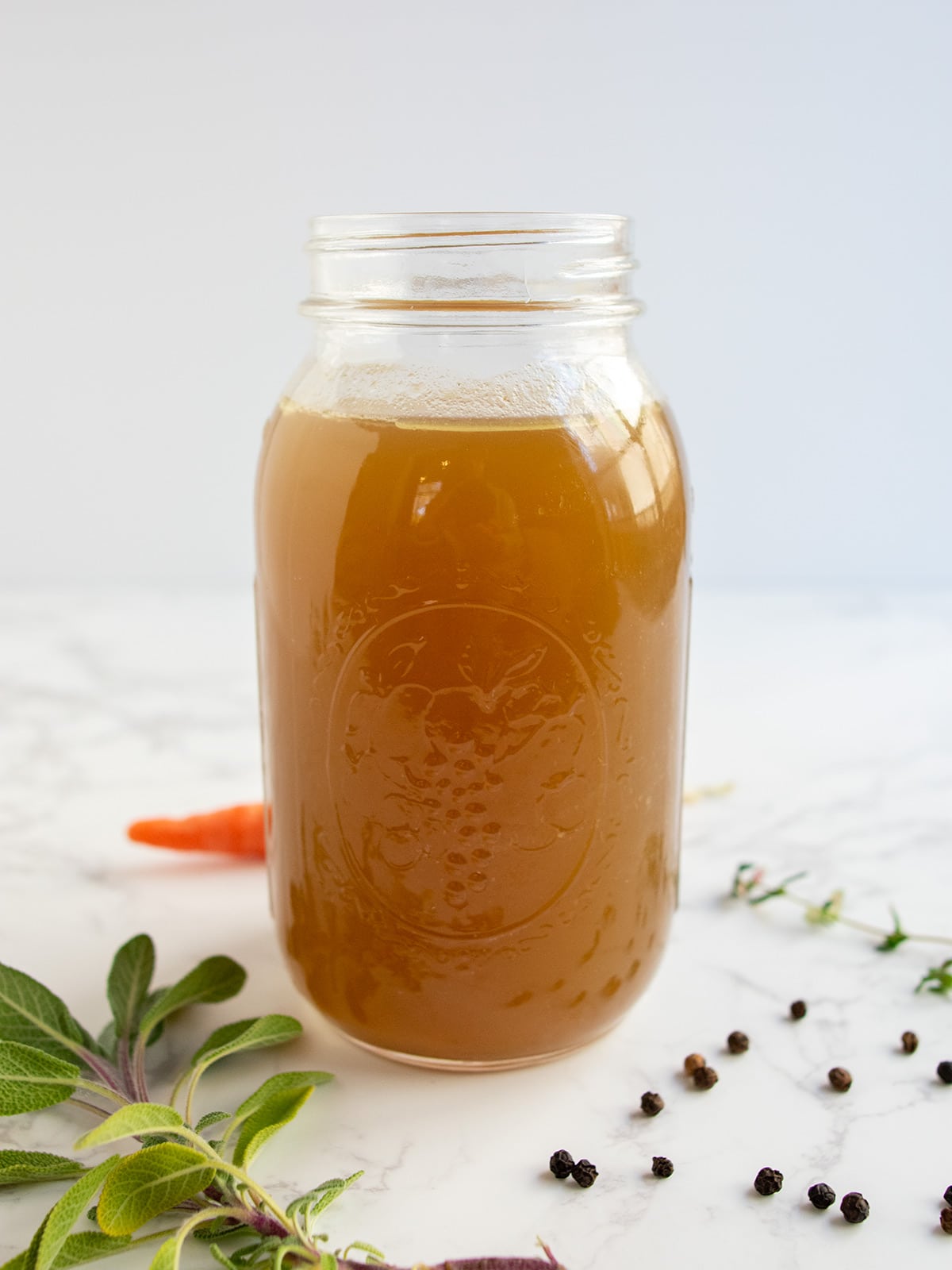 Close up of one bottle of turkey stock with herbs and a carrot nearby.