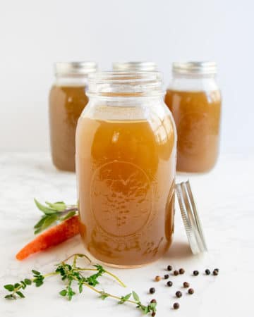 Several bottles of turkey stock with fresh herbs and a carrot.