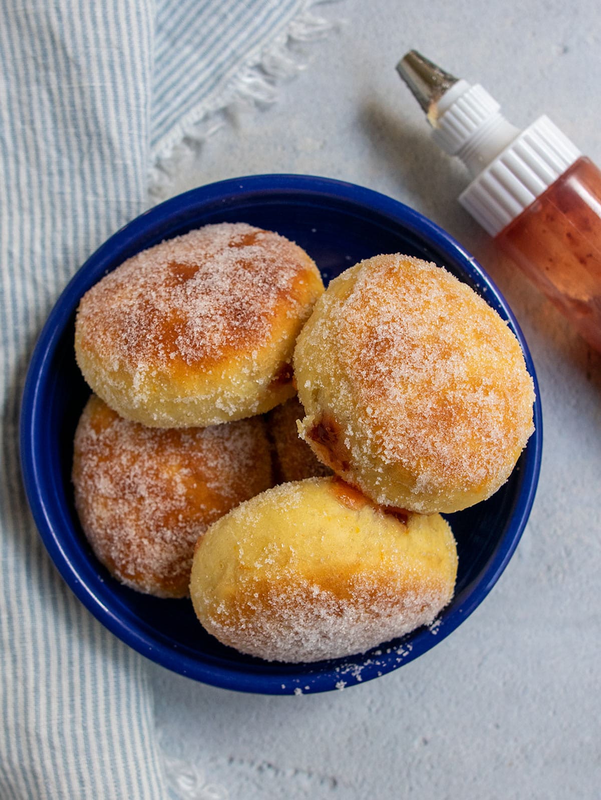 Baked sufganiyot in a blue bowl with a jam squeeze jar on the side.