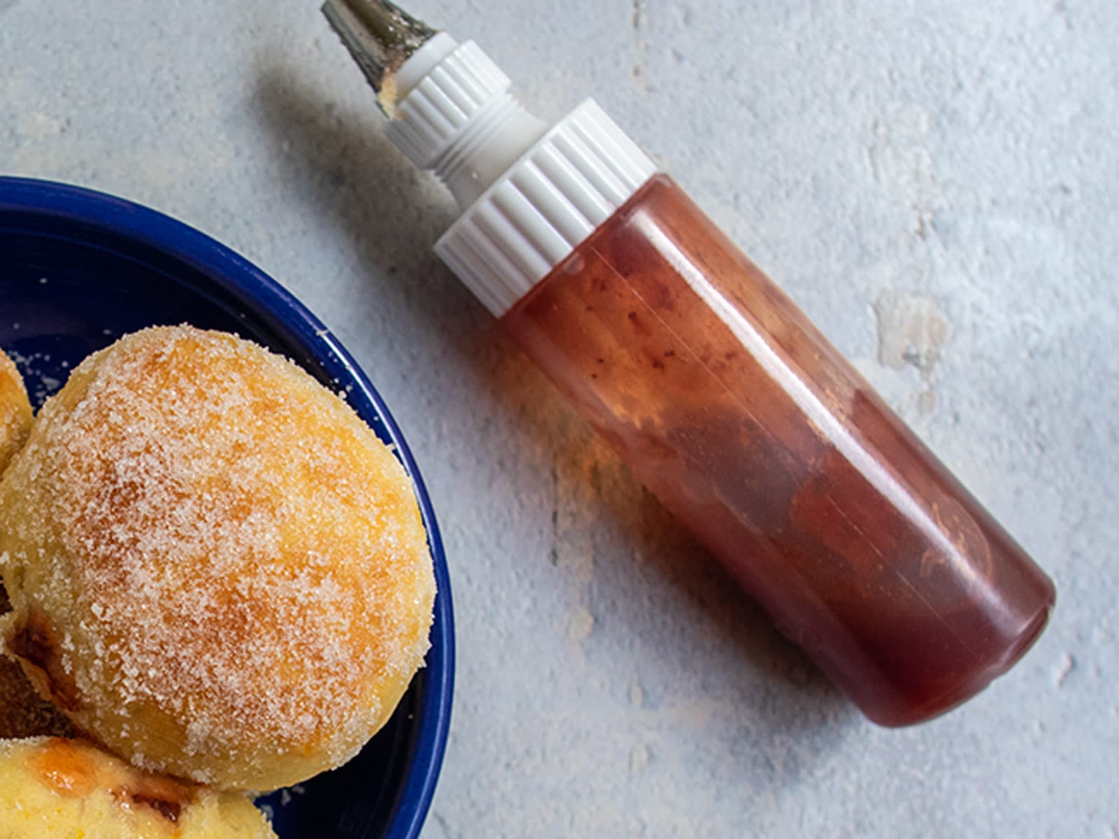 Jam in squeeze bottle next to a bowl of baked sufganiyot.