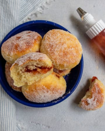 Baked sufganiyot in blue bowl with one cut open and a squeeze bottle of jam.