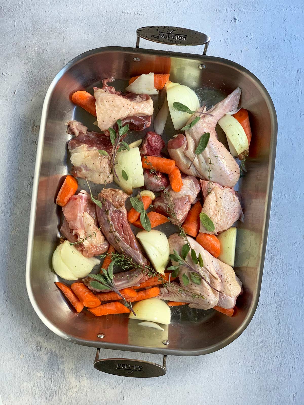 Raw turkey and vegetables and herbs in a large roasting pan.