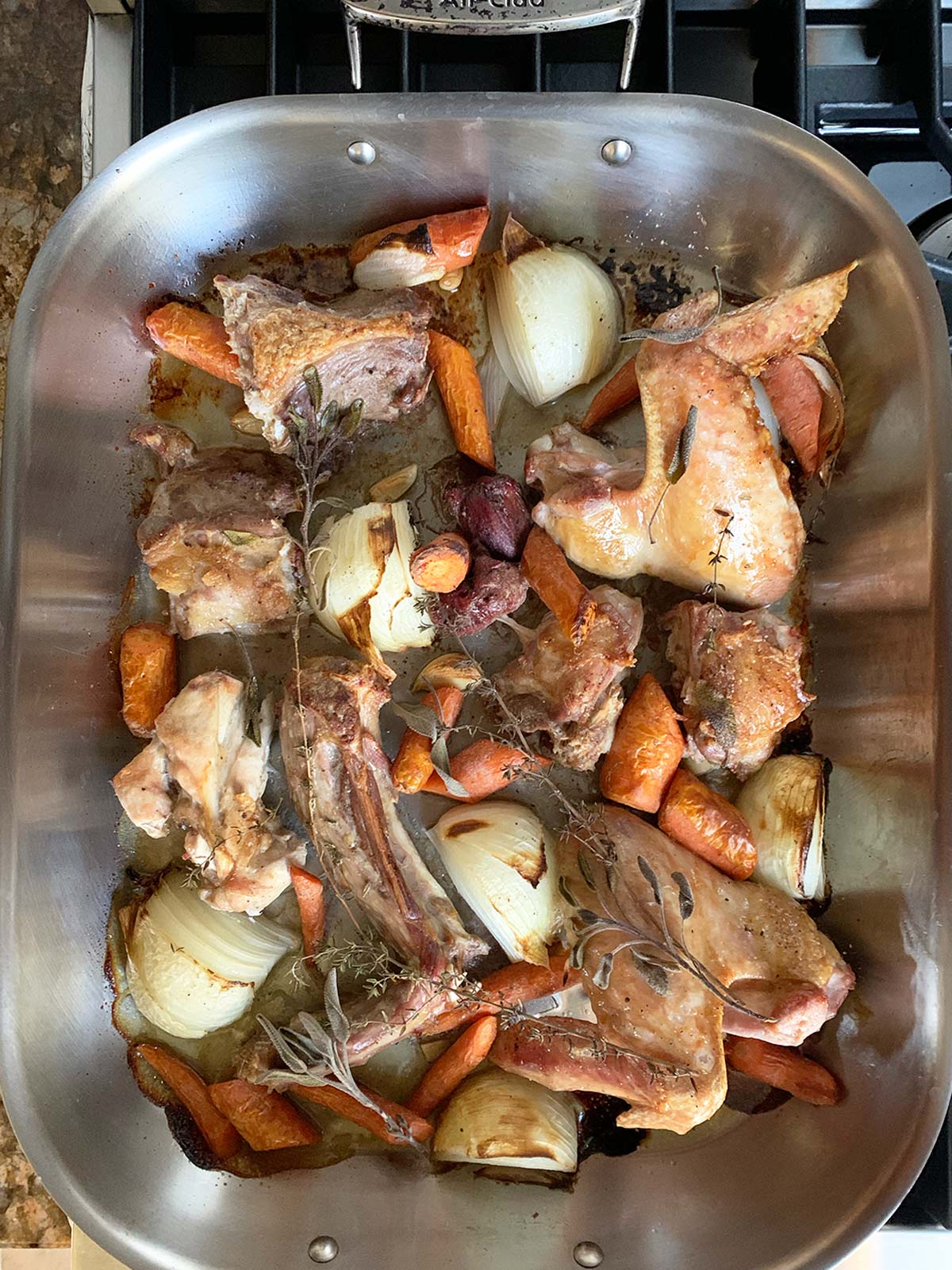 Roasted turkey parts and vegetables in large roasting pan after cooking.