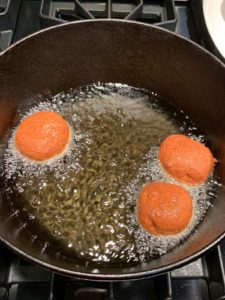 Three donuts in a cast iron pot frying in oil.