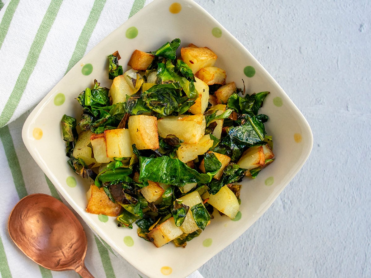 Croatian-style greens and potatoes (blitva) in bowl with a copper spoon with a striped napkin.