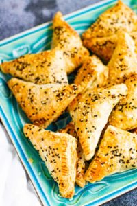Pastelicos or borekas with black and white sesame seeds on a blue plate.