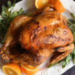 Roasted turkey on white platter with oranges and fresh sage.