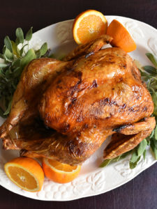 Roasted turkey on white platter with oranges and fresh sage.