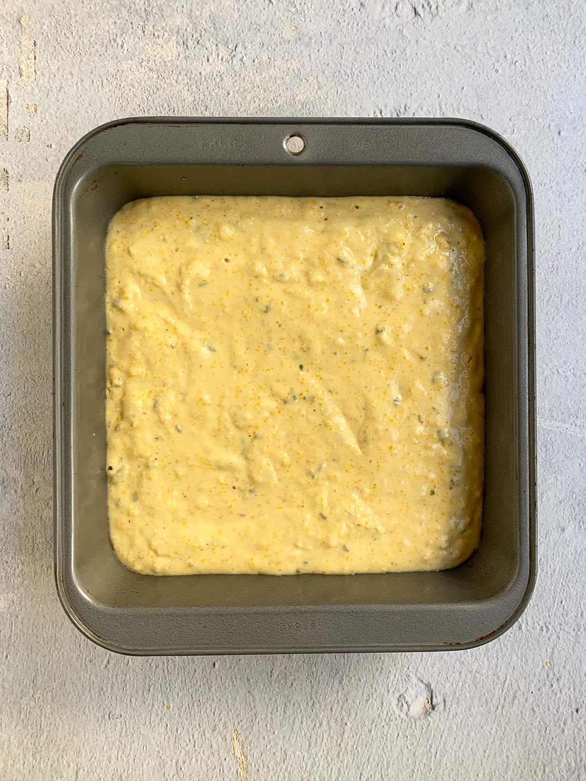 Honey cornbread batter in a grey square pan.