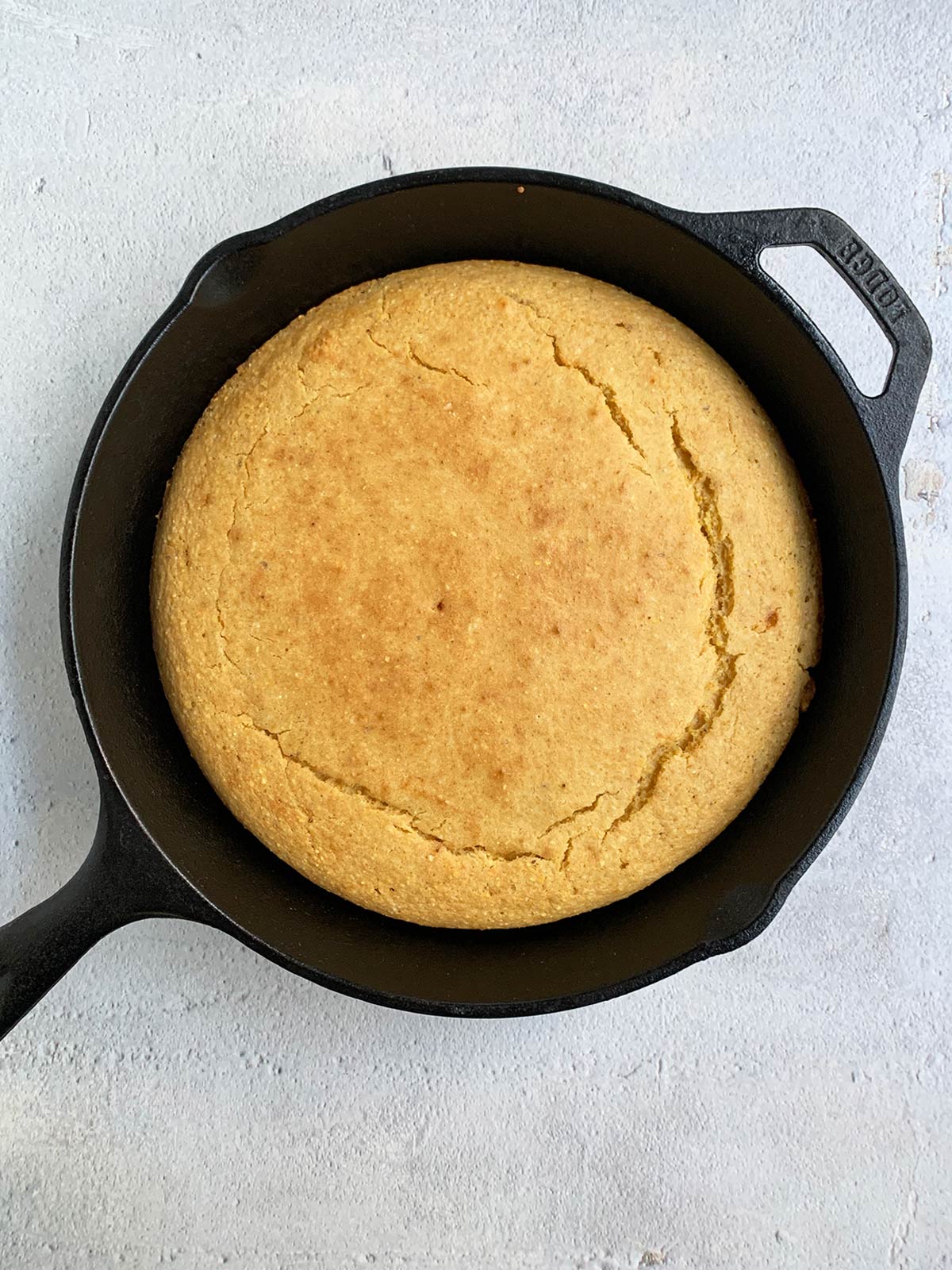 Dairy-free cornbread in a cast iron pan on a blue background.