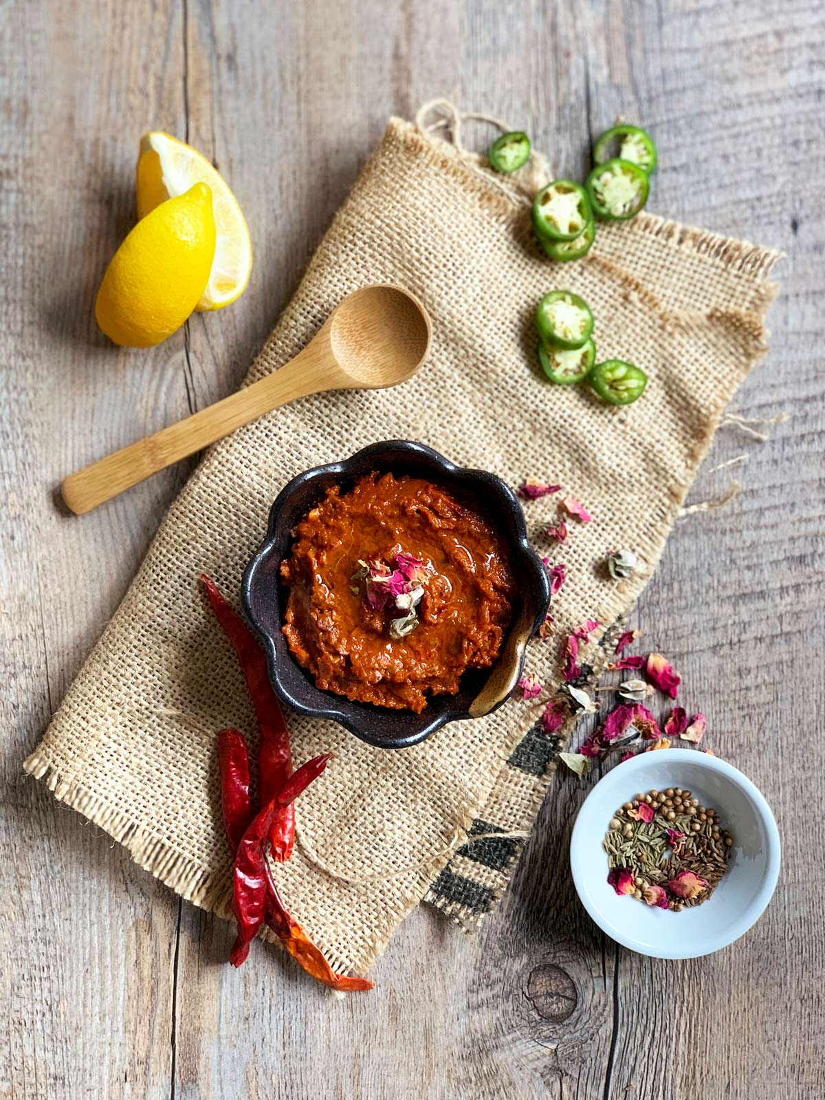 Rose harissa beauty shot on burlap with ingredients surrounding a brown bowl.