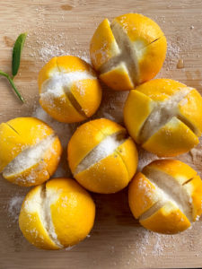Fresh lemons on a cutting board with slits cut in them filled with kosher salt.