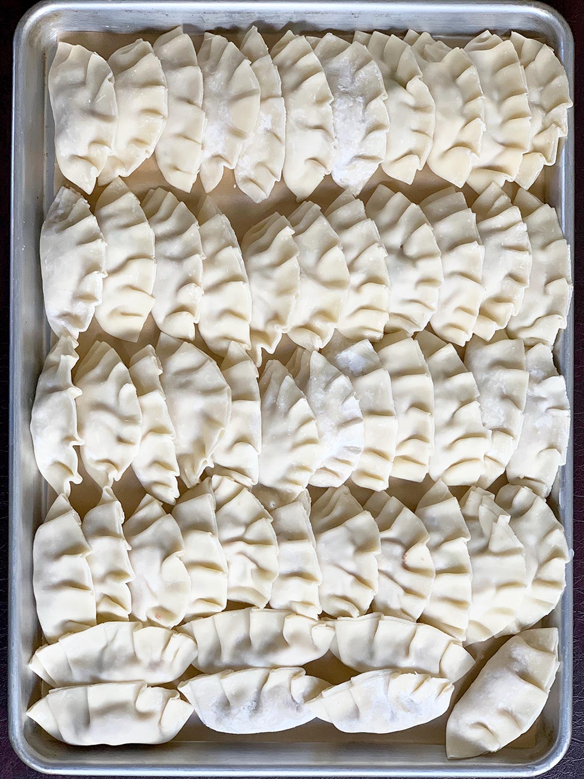 Uncooked mandu on a sheet tray ready to be cooked or refrigerated.
