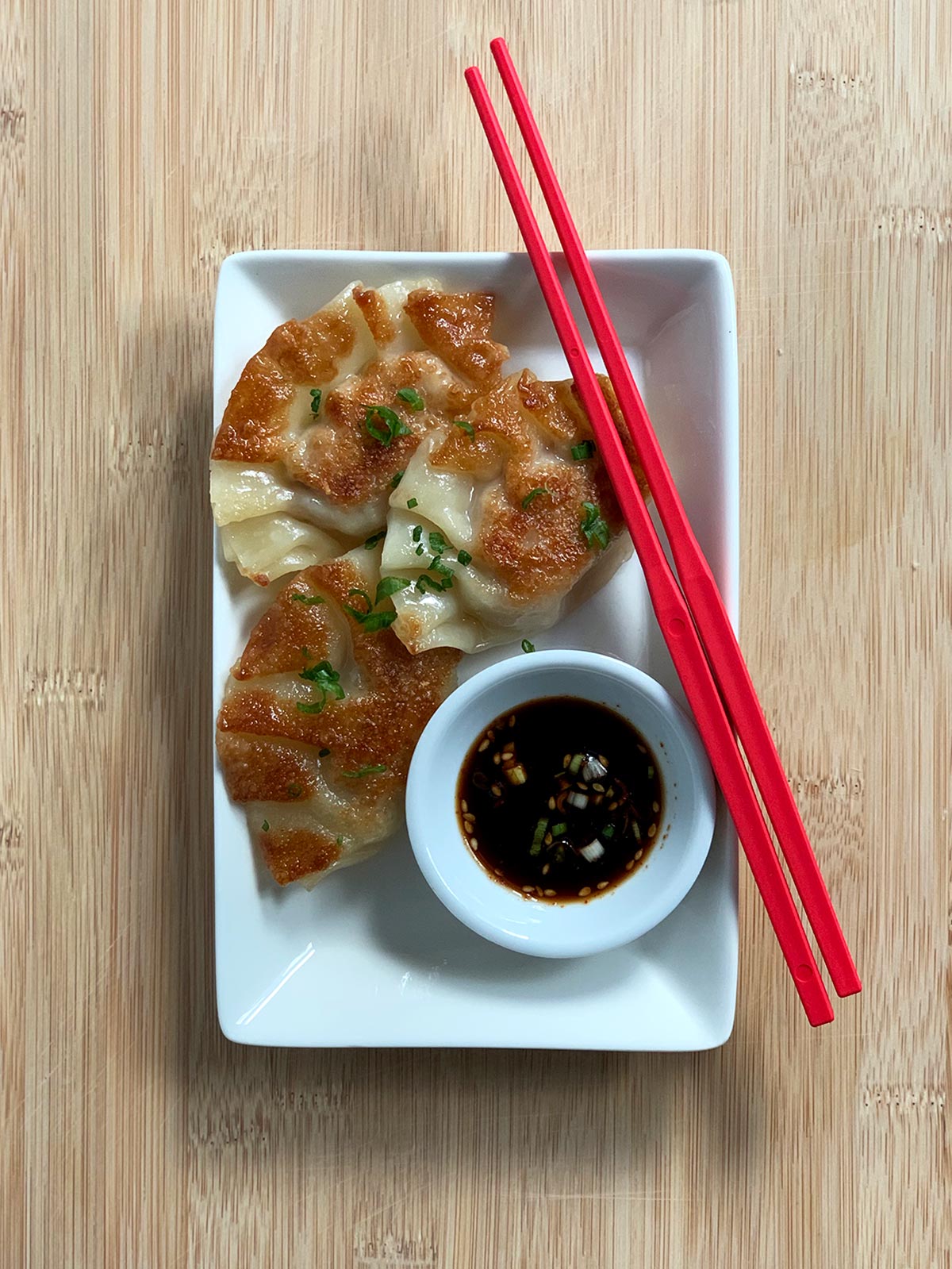 Fried mandu on a white plate with dipping sauce and red chopsticks.