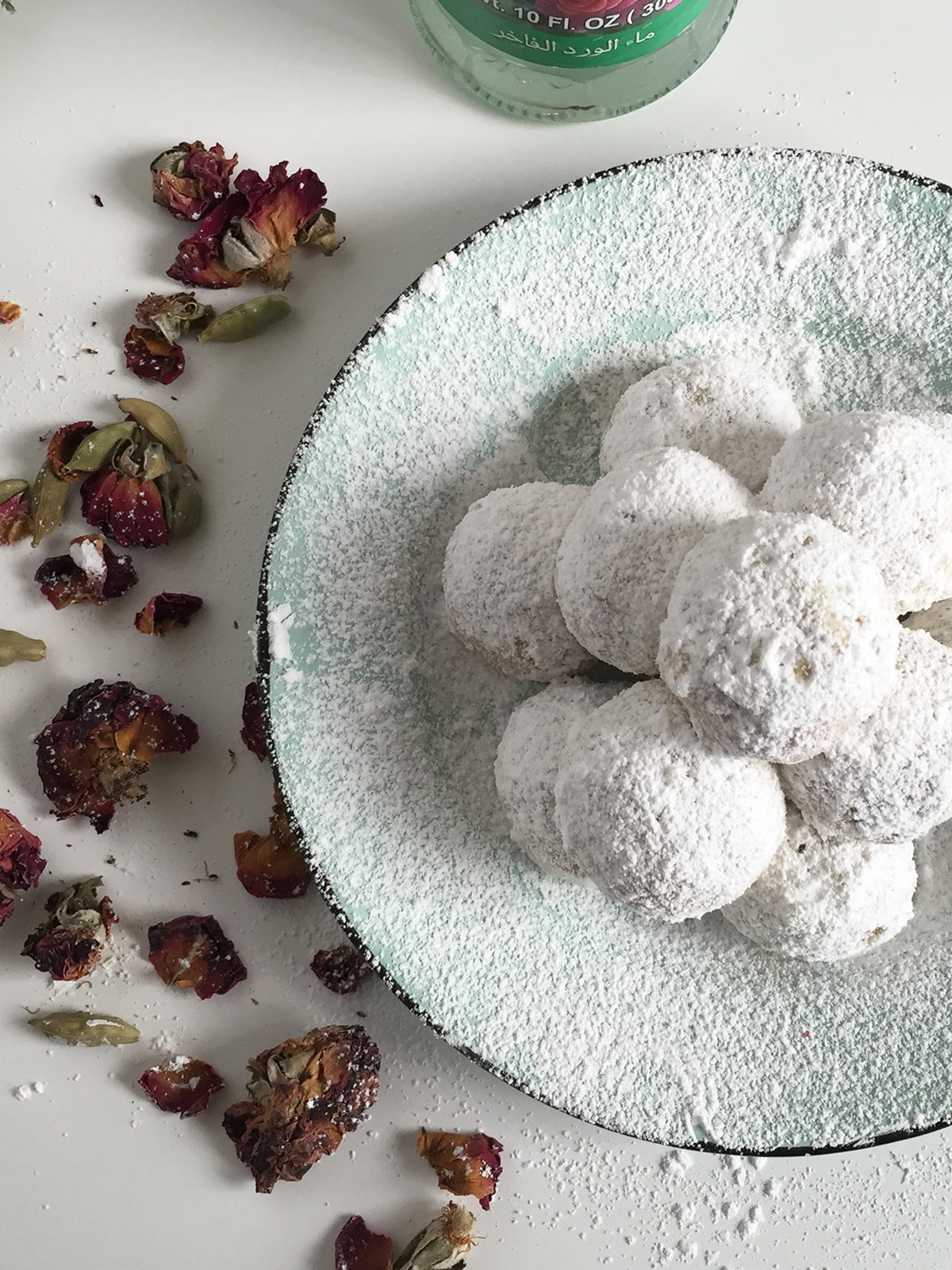 Pistachio snowballs cookies with rose and cardamom on a teal plate dusted with powdered sugar.